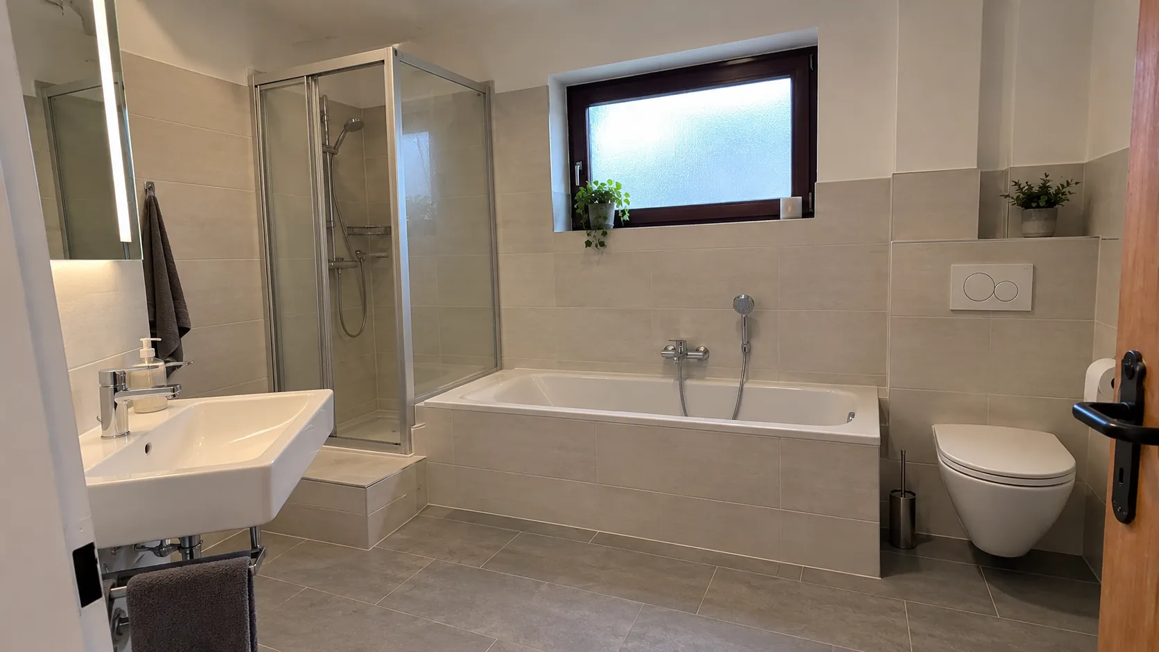Nachher: dasselbe Bad mit großformatigen Fliesen, neuer Wanne, Dusche und Wand-WC