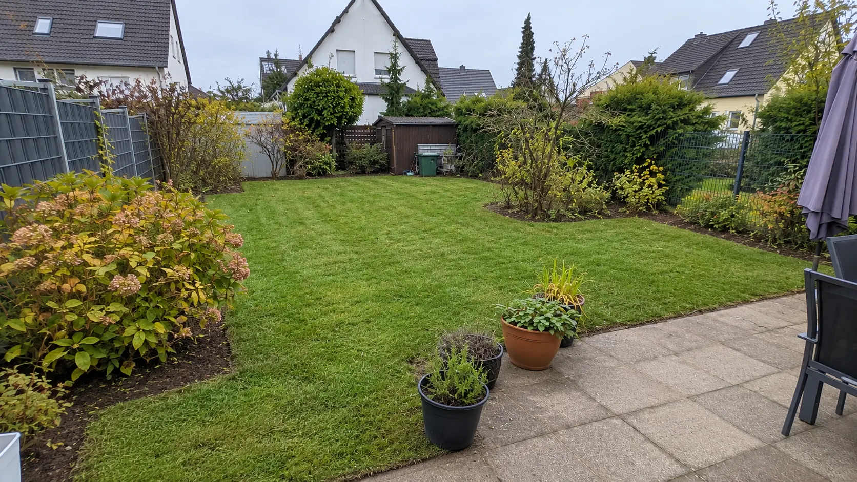 Nachher: derselbe Garten mit gemähtem Rasen, sauberen Beetkanten und freier Terrasse